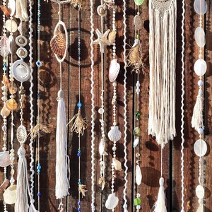May include: A wall hanging made of white macrame with seashells, beads, and dreamcatchers. The wall hanging is made of natural materials and has a bohemian style.