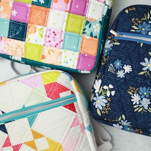 May include: Three colourful quilted bags with zip closures. One bag features a patchwork design with squares of various patterns and colours. Another has a floral pattern on a navy background. The third bag has a geometric design.