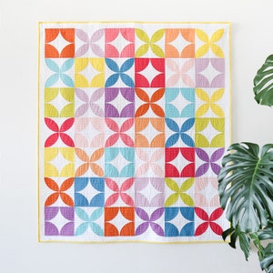 May include: A colorful quilt with a geometric pattern of overlapping circles and squares in shades of pink, orange, yellow, green, blue, and purple. The quilt is made with a white background and has a yellow border.