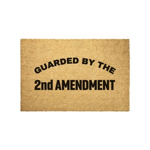 May include: A brown doormat with the text "GUARDED BY THE 2nd AMENDMENT" in black.