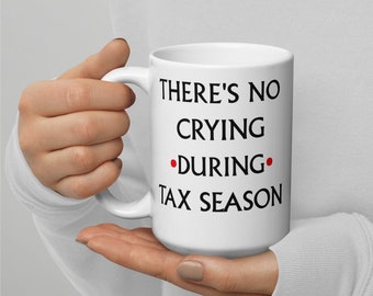 May include: White ceramic mug with black text that reads "There's no crying during tax season".