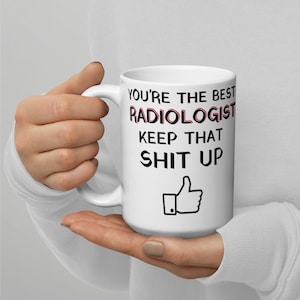 以下が含まれることがあります： 白いセラミック製のコーヒーカップで、黒い文字で「You're the best Radiologist Keep that Shit Up」と書いてあり、親指を立てたアイコンが付いています。