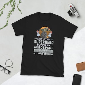 May include: Black t-shirt with a graphic of a person in a flight suit standing in front of a plane with the text "I may not be a superhero but I'm an aerospace engineer so close enough."