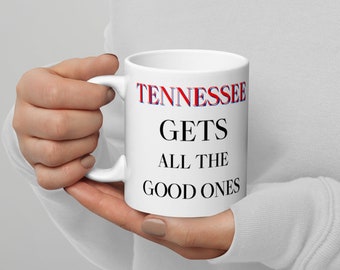 Puede incluir: Taza de cerámica blanca con el texto "Tennessee Gets All The Good Ones" en letras rojas y azules.