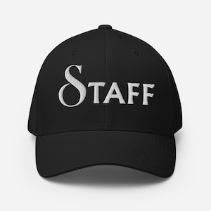 以下が含まれることがあります： 前面に白い糸で「STAFF」という文字が刺繍された黒い野球帽。この帽子は構造化されたクラウン、カーブしたつば、中央上部にボタンを備えています。文字にはセリフ体フォントが使用されており、大きなSの文字が特徴です。