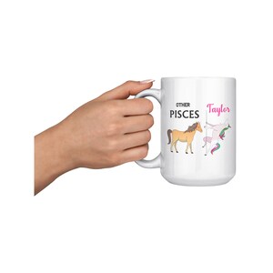 Könnte beinhalten: Eine weiße Keramiktasse mit einer Schwarzweißillustration eines Pferdes und eines Einhorns. Der Text "Other Pisces" und "Taylor" ist auf der Tasse aufgedruckt.
