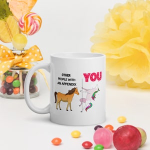 Puede incluir: Taza de cerámica blanca con una ilustración humorística de un caballo y un unicornio. El texto en la taza dice "Other people with an appendix" y "You".