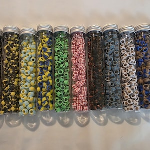 May include: Eleven clear plastic cylindrical tubes filled with small, round, patterned beads. Each tube contains a distinct color combination, including black, yellow, green, pink, blue, and brown, all topped with a silver-colored metal screw cap.