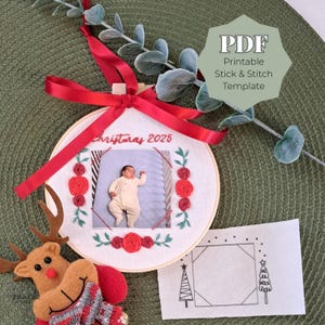 Puede incluir: Adorno navideño bordado con foto de bebé, cinta roja y el texto "Christmas 2025". El adorno está decorado con rosas rojas y hojas verdes. Se incluye una plantilla PDF.
