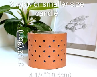 May include: A cylindrical tan leather candle sleeve featuring a perforated polka dot pattern. The sleeve measures 3 1/2 inches in height and 4 1/4 inches in diameter. Text on the image states: Fits B & BW 3 wick or smaller size candle.