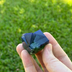 May include: A deep blue and green fluorite crystal with a geometric shape.