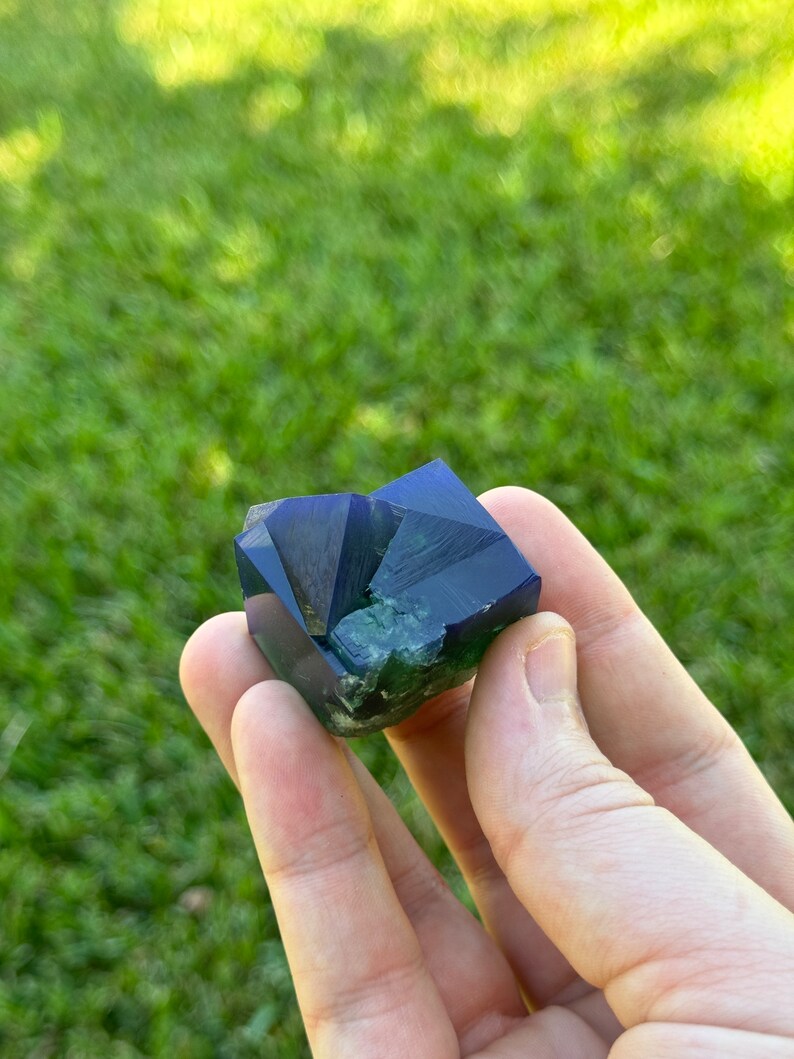 May include: A deep blue and green fluorite crystal with a geometric shape.