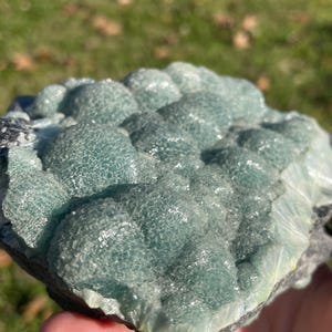 May include: A raw mineral specimen featuring a cluster of rounded, botryoidal formations in a translucent seafoam green hue. The surface displays a crystalline, textured appearance with visible light refraction across the bubbly, dome-shaped structures.