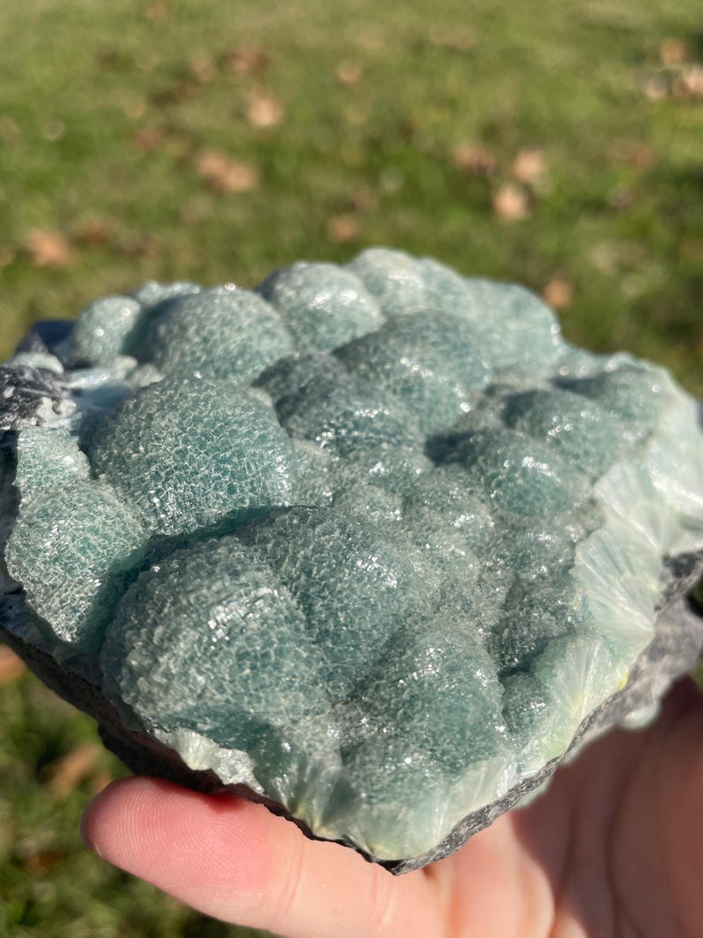 May include: A raw mineral specimen featuring a cluster of rounded, botryoidal formations in a translucent seafoam green hue. The surface displays a crystalline, textured appearance with visible light refraction across the bubbly, dome-shaped structures.