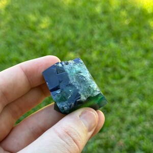 May include: A dark blue and green fluorite crystal with a rough, natural texture. The crystal is a geometric shape with many facets.