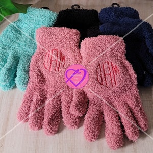 May include: Three pairs of fuzzy gloves in pink, blue, and black. The pink gloves have the monogram "JAM" embroidered on them in red thread.