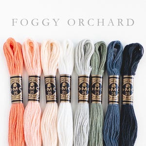 Text at the top of the image reads "FOGGY ORCHARD". Eight skeins of embroidery floss are shown below the text. The colors of the floss range from peach to dark gray.