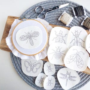 May include: A set of embroidery patterns featuring various insects, including a butterfly, dragonfly, ladybug, and beetles. The patterns are printed on white fabric and are ready to be stitched.