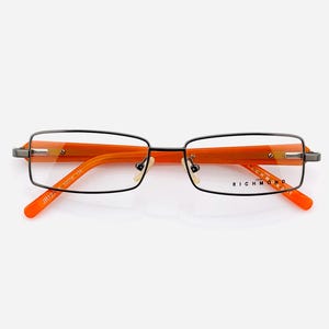 May include: Rectangular eyeglasses with black frames and orange temples. The glasses have clear lenses and the brand name "RICHMOND" is visible on the right temple. The overall design is modern and stylish.