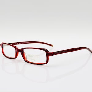 May include: Red plastic framed spectacles with clear lenses. The frame has a subtle curve and the arms are thin. The text "LIMITED COLOUR OF PRODUCTION" is printed on the right lens.