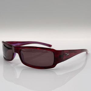 May include: Burgundy-coloured sunglasses with a dark grey lens. The sunglasses have a silver logo that says "SKY-08" on the right side and a silver "X" on the right arm.