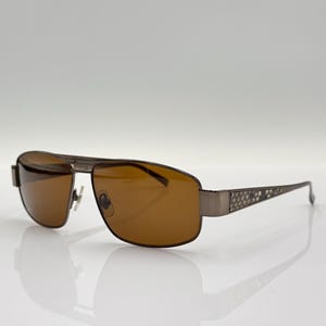 Può includere: Un paio di occhiali da sole aviator marroni con montatura in metallo e un motivo testurizzato sulle aste.