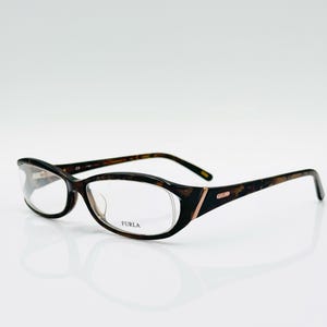 May include: A pair of eyeglasses with a tortoiseshell pattern on the frames and arms. The glasses have an oval shape and clear lenses. The brand name "FURLA" is visible on the lens.