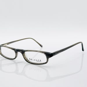 May include: Rectangular eyeglasses with a striped pattern in shades of gray and black. The frames have a subtle texture, and the temples are thin and dark. The brand name "CELESTE" is printed on the temple.