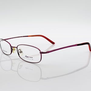 Puede incluir: Gafas con una montura fina y rectangular en un tono púrpura oscuro. Las patillas transicionan de púrpura a rojo y naranja. Las lentes son transparentes y el nombre de la marca es visible.