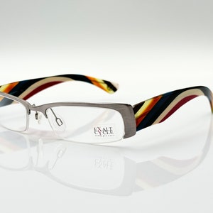 Può includere: Occhiali color argento con asta a righe multicolori. Il nome del marchio "EXALT EYEWEAR" è stampato sulla montatura.
