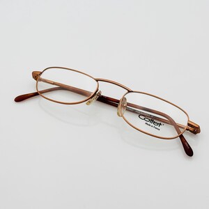 Puede incluir: Gafas con montura de metal dorado y patillas marrones. Las lentes son transparentes y las gafas tienen forma ovalada. La marca "Cottet" es visible en la montura. Fabricado en Francia.