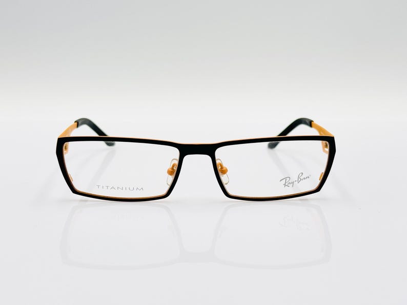 K&ouml;nnte beinhalten: Schwarze und goldene Titan-Gestellbrille mit Ray-Ban-Branding auf der rechten Linse.