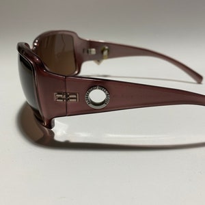 May include: Burgundy-coloured sunglasses with a silver metal frame and the text "ALESSANDRO DELL'ACQUA" on the side.