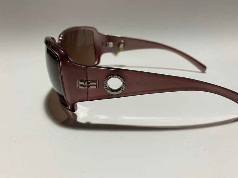 May include: Burgundy-coloured sunglasses with a silver metal frame and the text "ALESSANDRO DELL'ACQUA" on the side.