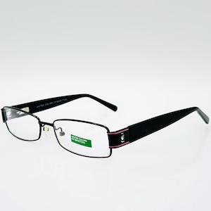 Puede incluir: Gafas rectangulares negras con lentes transparentes. Las monturas son negras con un fino acento rosa en las patillas. La marca "UNITED COLORS OF BENETTON" es visible en la patillas. Las gafas están sobre un fondo blanco.