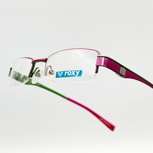 Puede incluir: Gafas sin montura rosa y verde con un logotipo Roxy azul en el marco.