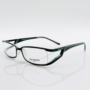 May include: Black eyeglasses with a modern design. The frames are black with a unique angular shape around the lenses. The brand name "ENOX" is visible on the frame. The glasses are set against a white background.