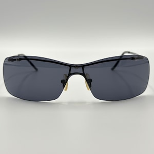 May include: Rimless sunglasses with dark gray lenses and a black metal frame. The sunglasses have a sleek, modern design with a subtle nose bridge and temples. The lenses are rectangular and provide a stylish look.