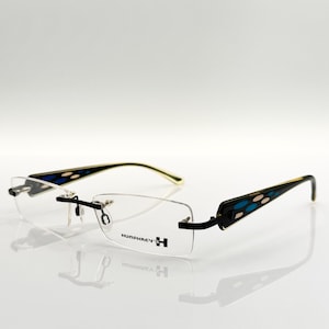 Puede incluir: Gafas sin montura negras y doradas con un diseño estampado azul y beige en las patillas. El nombre de la marca "Humphrey H" está impreso en la montura.