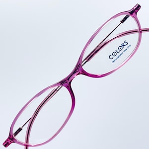 May include: Pink oval-shaped eyeglasses with thin metal arms and the word "COLORS" printed on the right lens. The text below "COLORS" reads "Demonstration Lens Only".