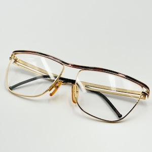 Peut inclure: Lunettes de vue dorées avec un pont noir et des accents marrons sur la monture.