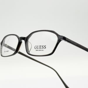 May include: Black plastic framed eyeglasses with a rectangular lens shape. The frames have the word "GUESS" printed on the side and "DEMO LENS ONLY" printed on the right lens.