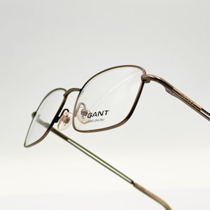 May include: Brown metal framed glasses with clear lenses. The glasses have the word "GANT" printed on the right lens.