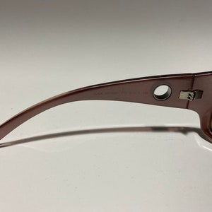 May include: A pair of brown sunglasses with a silver hinge and a round hole on the side of the frame. The sunglasses have a brown lens and the text "GUCCI MOD. 4125/S CE 52" is printed on the frame.