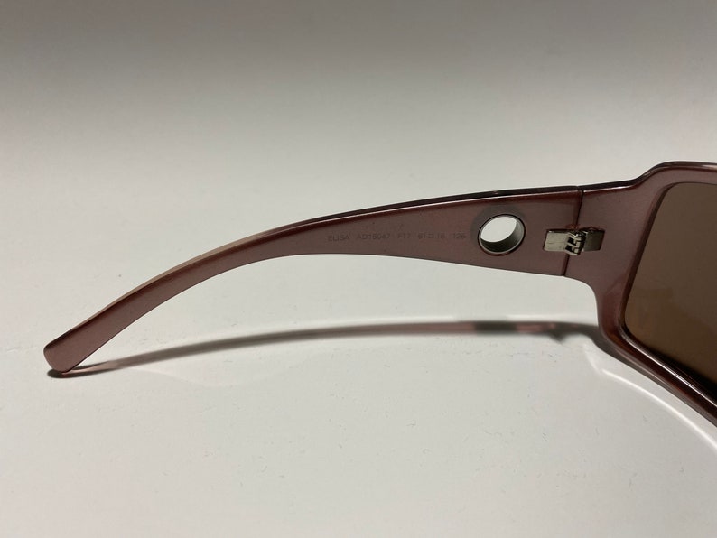 May include: A pair of brown sunglasses with a silver hinge and a round hole on the side of the frame. The sunglasses have a brown lens and the text "GUCCI MOD. 4125/S CE 52" is printed on the frame.