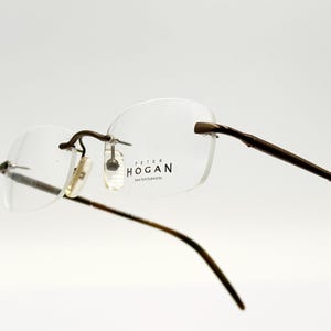 May include: Brown rimless eyeglasses with a Peter Hogan Eye Wish Essentials label on the right lens.