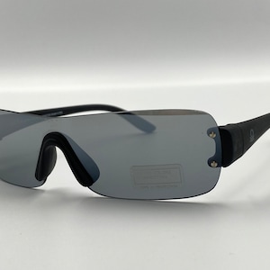 Peut inclure: Lunettes de soleil noires avec des verres miroir et une monture noire. Les lunettes ont un design unique avec un dessus plat et un bas incurvé.