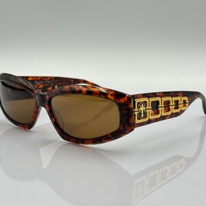 May include: Tortoiseshell sunglasses with gold accents and a chain detail on the arms.