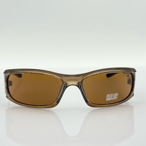 May include: Brown-tinted sunglasses with a wraparound design. The frames are a translucent brown color, and the lenses are a darker brown. The text "KILLER LOOP" is visible on the right lens. The sunglasses are set against a white background.