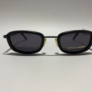 May include: Black rectangular sunglasses with dark lenses and a gold "SONIA RYKIEL" label on the right lens.